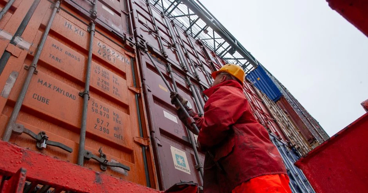 Industrial worker securing cargo containers on a rainy day at a shipping port.